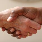 Two people shaking hands in a friendly greeting, with one person wearing a watch and ring