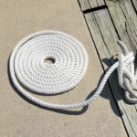 A white rope coiled in a neat spiral on concrete next to a wooden dock with rope cleats