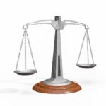 A silver balance scale with two empty pans hanging from chains on a wooden base, used to weigh and compare objects