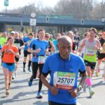 A group of runners of all ages participating in a marathon race, wearing colorful athletic clothes and numbered race bibs.