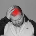 A man holding his forehead with his hand, with a red area showing where he has a headache or pain in his head.