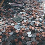 Hundreds of coins and dollar bills scattered across a dark surface, showing different types of money including pennies, nickels, dimes and quarters.