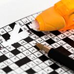 Orange correction tape being used to fix mistakes on a crossword puzzle with black and white squares and letters