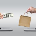 Two laptop computers with hands reaching out - one hand holds money and the other holds a shopping bag, showing online buying and selling