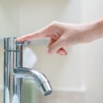 A hand reaching to turn on a shiny chrome water faucet in a bathroom or kitchen sink