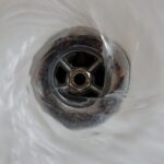 A close-up view looking down into a white bathtub drain with a dark metal stopper and chrome fixture in the center.