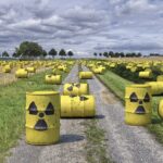 A field filled with hundreds of yellow barrels marked with radioactive warning symbols scattered across green grass under a cloudy sky.