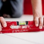 Hands holding a red spirit level tool with a green bubble in the center to check if surfaces are straight and even