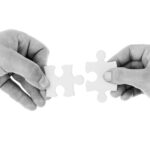 Two hands bringing puzzle pieces together to connect them, showing teamwork and cooperation