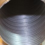 Looking down into a round metal pipe or tube with ridged spiral grooves running along the inside walls