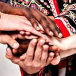 Several hands of different skin colors stacked together in a team huddle, showing cooperation and friendship.