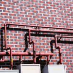 Red pipes and valves mounted on a brick wall with repeating square patterns