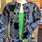 A black and white patterned jacket with many different designs displayed on a white mannequin in a sewing room