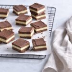 Layered chocolate dessert squares with white cream filling cut into neat pieces on a wire cooling rack