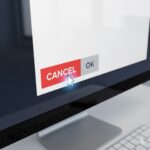 A computer screen showing two buttons - a red CANCEL button and a gray OK button, with a mouse cursor pointing at the CANCEL button.