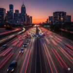 A busy highway at sunset with red and white light trails from cars driving toward tall city buildings in the distance